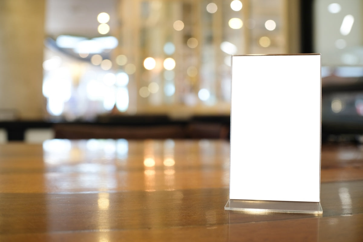 Vertical clear acrylic menu holder with magnetic edges displayed on a restaurant tabletop, showing double-sided insert visibility.