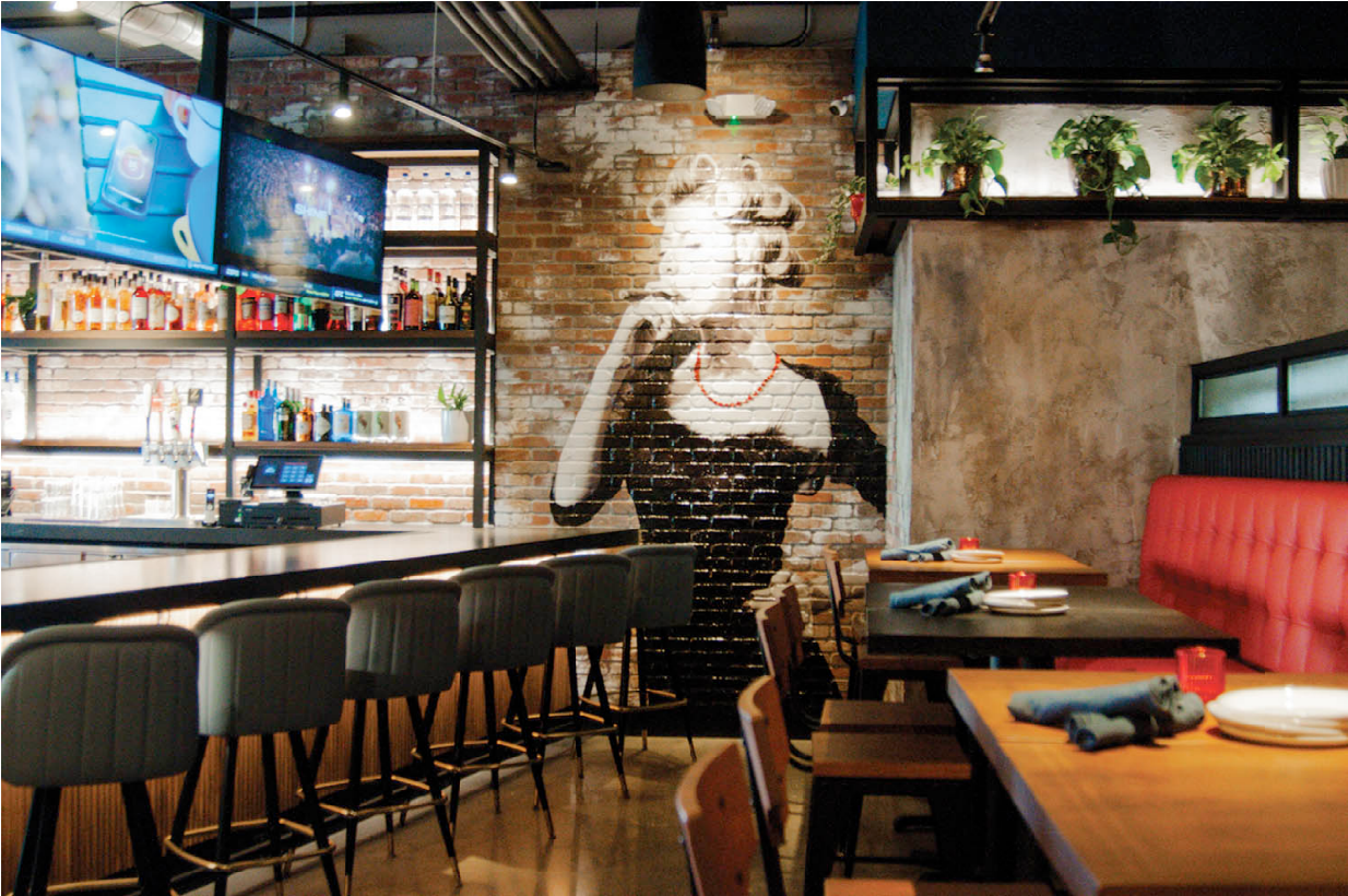 Modern restaurant interior with brick wall, bar area, and red booth.