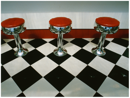 Three red and chrome bar stools on a black and white checkered floor.