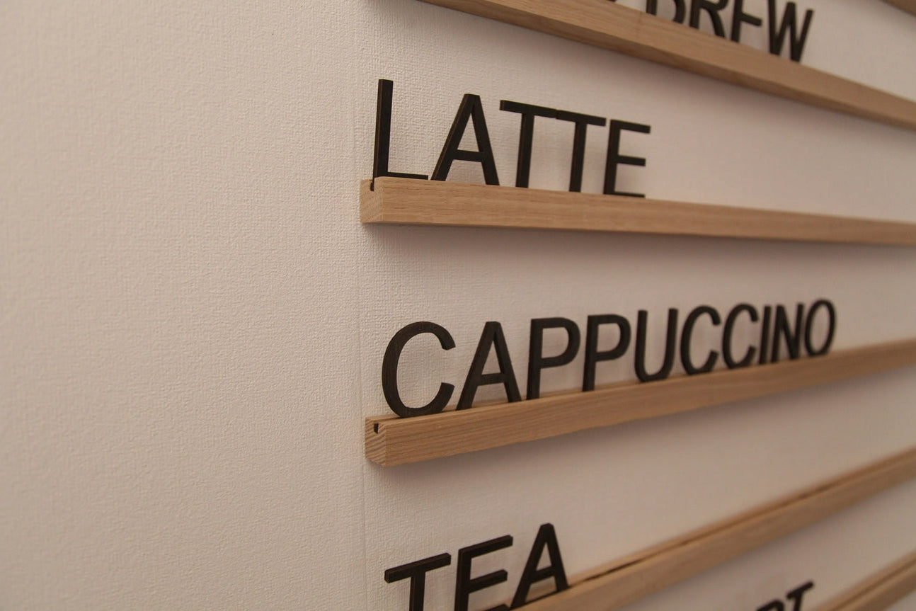 Wood wall-mounted menu rail set in natural ash with black changeable letters arranged on the rails.