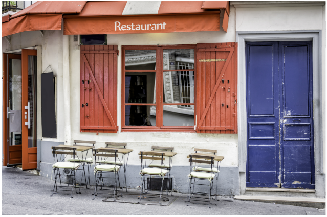 Restaurant exterior with outdoor seating area, red awning, and blue door.