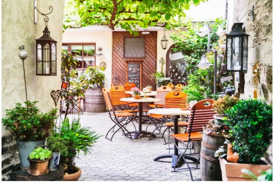 Outdoor patio with tables, chairs, and potted plants in a garden setting.