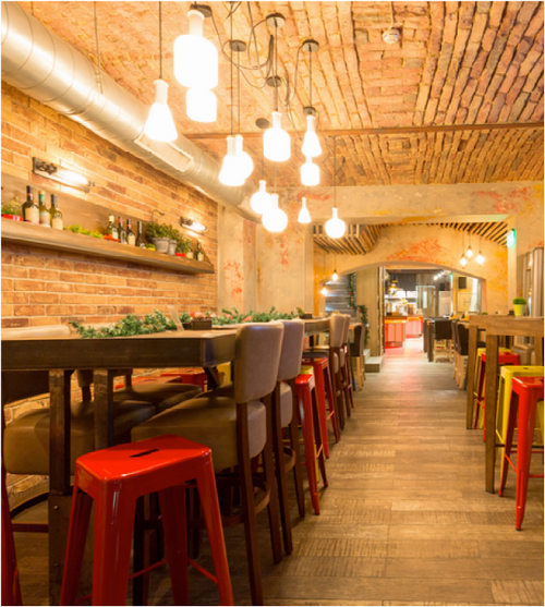 Modern restaurant interior with wooden floors, brick walls, and pendant lights.