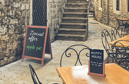 Outdoor cafe setting with tables, chairs, and chalkboard signs advertising a special offer and happy hours.