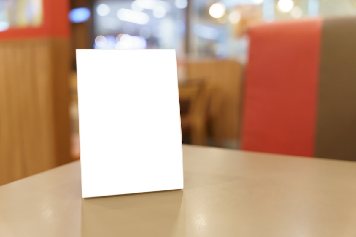 Clear slant back acrylic menu holder with magnetic closure displayed on a restaurant tabletop, showing double-sided menu visibility.