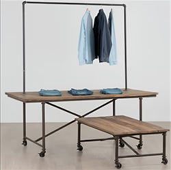 Front view of a vintage industrial display table made of elm wood and iron, showing the rectangular top and locking caster wheels used for merchandising in retail or hospitality spaces.